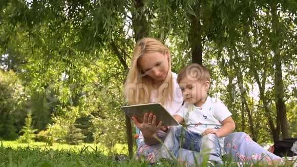 快乐的妈妈和她的小儿子在公园里玩平板电脑慢动作视频的预览图