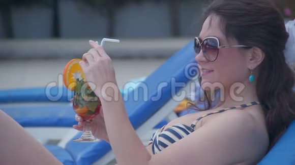 美丽的年轻女性在阳光明媚的海滩上用新鲜的鸡尾酒放松视频的预览图