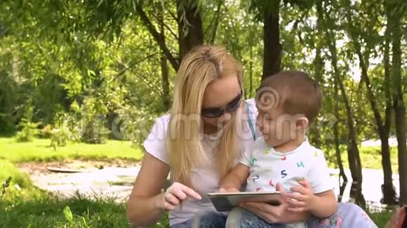 快乐的妈妈和她的小儿子在公园里玩平板电脑慢动作视频的预览图