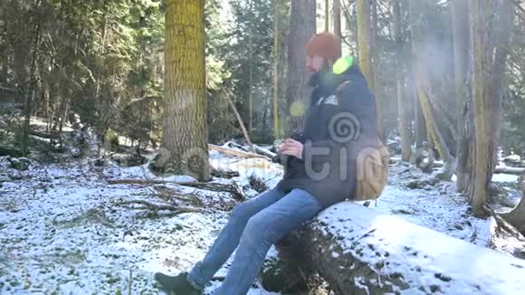 一位留着胡子的男性旅行者摄影师在冬天的森林里用他的相机拍摄大自然的照片旅行概念视频的预览图