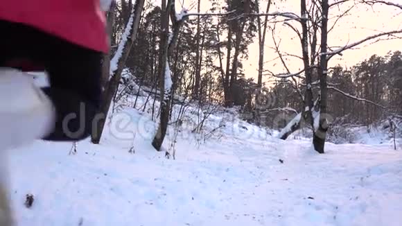 穿红色夹克的苗条女孩在冬天森林里从镜头里跑出来的慢动作视频视频的预览图