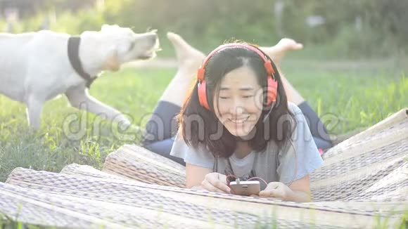 女人喜欢用耳机听音乐在户外和友好的狗一起玩耍视频的预览图