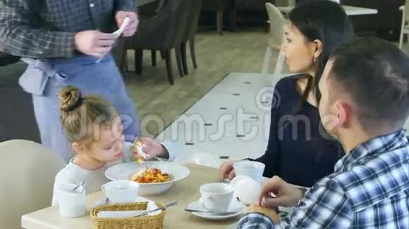 有趣的小女孩在和父母一起在咖啡馆吃晚饭前玩玩具服务员给她拿了一个塞子视频的预览图