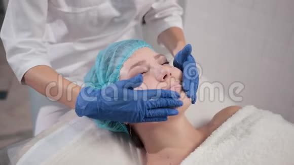 带蓝色手套的护士医生用轻动作做女性面部按摩视频的预览图