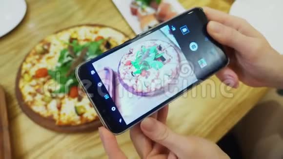 特写镜头女手在餐厅的智能手机上拍披萨视频的预览图