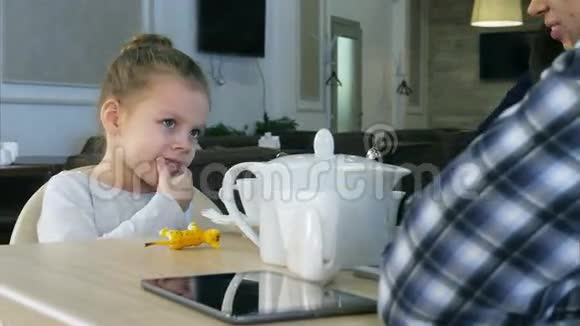 小金发女孩和她可爱的父母坐在咖啡馆里喝茶视频的预览图