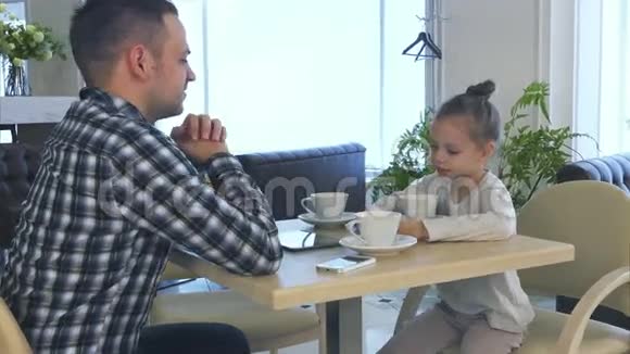 父亲和女儿在咖啡馆等妈妈女人用可爱的微笑说话视频的预览图