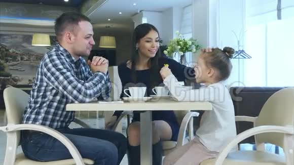快乐的年轻父母在他们的家庭度假期间在咖啡馆喝茶聊天视频的预览图