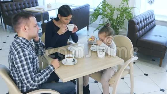 父亲和妻子和女儿坐在咖啡馆或餐馆里打电话妈妈看着他生气视频的预览图