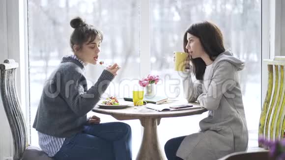 两个年轻的大学生女孩在咖啡馆里吃饭聊天视频的预览图