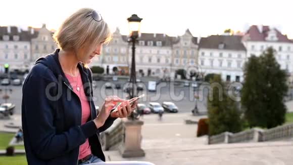 女人坐在户外用智能手机视频的预览图