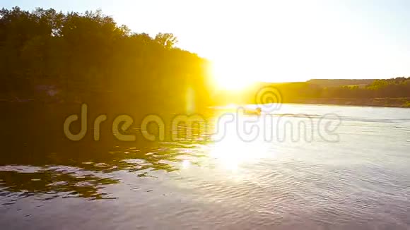 摩托艇在美丽的阳光下漂浮在河上日落时游艇的轮廓在河上漂浮视频的预览图