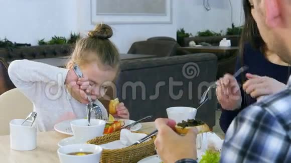 家人在餐馆吃健康的午餐小女儿吃白面包的蔬菜沙拉视频的预览图