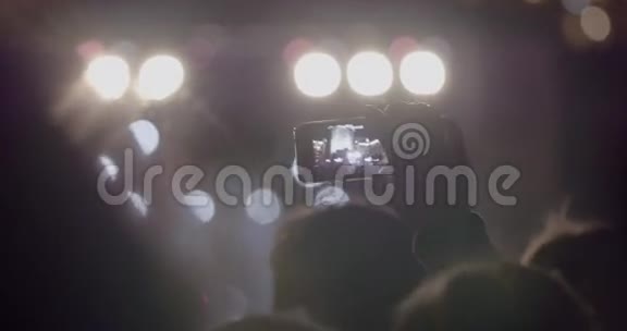 观众在室外音乐音乐会上通过智能手机在明亮的聚光灯前录制舞台视频视频的预览图