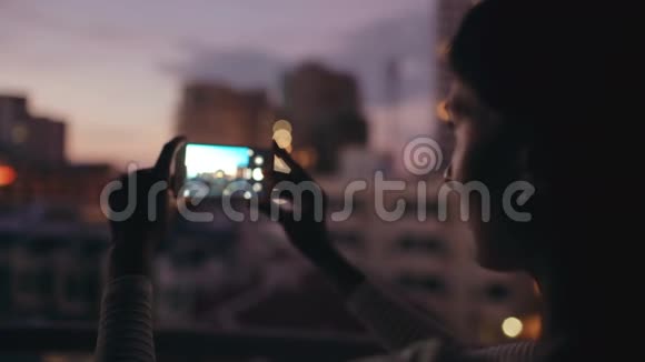 夜间在酒吧屋顶露台用智能手机拍摄城市景观的特写镜头视频的预览图