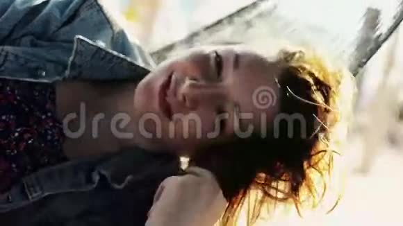 快乐的年轻女孩在沙滩上的吊床上摇摆在镜头中微笑晴天摇动头发视频的预览图