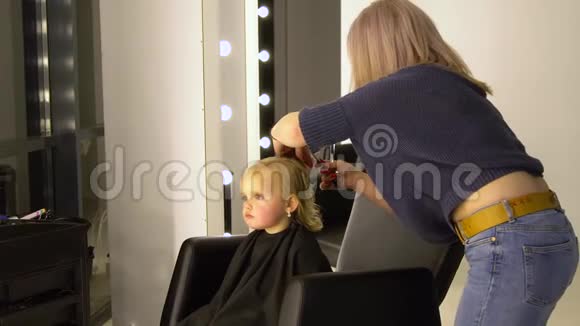 一个在美容院的小孩漂亮的女孩坐在椅子上理发师剪了她的头发孩子是视频的预览图