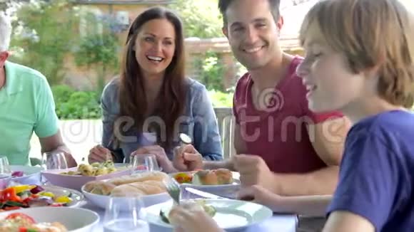 坐在户外围着桌子吃饭的多代家庭视频的预览图