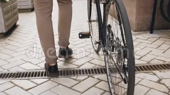 低角度慢动作镜头时尚男子与老式运动自行车行走在街道与铺砌的道路视频的预览图
