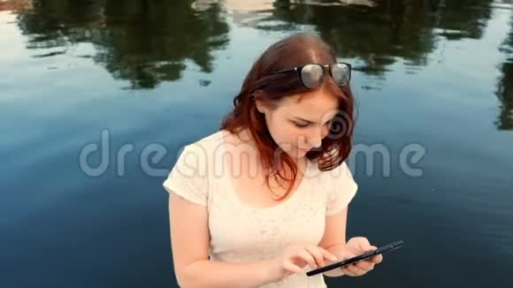 一位年轻的女士在河边的一个美好的春天在公园里玩平板电脑一边在户外放松视频的预览图