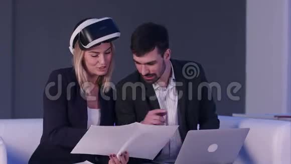 女建筑师戴着虚拟现实耳机用笔记本电脑向男同事展示设计图视频的预览图