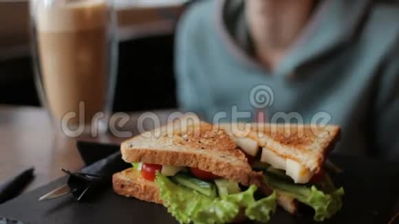 黑色托盘上有奶酪和蔬菜的美味三明治女人吃早餐视频的预览图