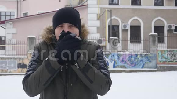 戴着黑帽子的年轻人在寒冷的冬天天气里暖手的肖像快关门户外活动视频的预览图