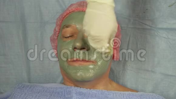 戴手套的女性美容师在男性客户的脸上戴上带刷子的泥面罩视频的预览图