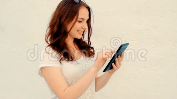 面带微笑的女学生拿着数码平板站在墙前看着屏幕视频的预览图