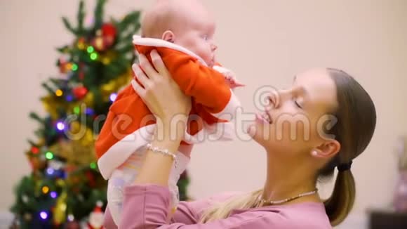 快乐的母亲和可爱的女婴在圣诞树的背景下视频的预览图