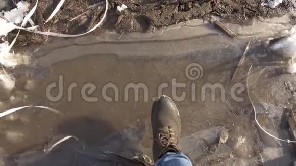 穿靴子的人的脚在泥泞的水坑上结冰视频的预览图