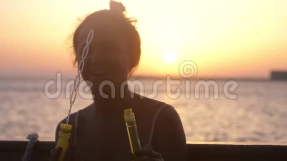 在美丽的夕阳下快乐的黑发女人在游轮上吹肥皂泡慢动作3840x2160视频的预览图