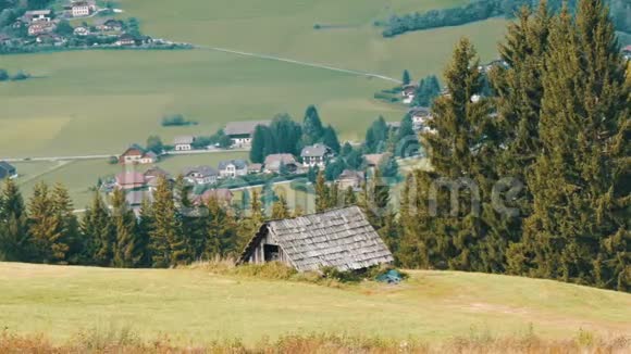 在奥地利阿尔卑斯山的一座小山上一座古老的老式木屋在新的现代建筑的背景下长满了绿草视频的预览图