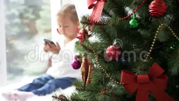 装饰的基督弥撒树和小女孩与智能手机的背景视频的预览图