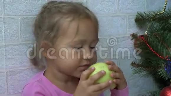 可爱的小女孩坐在地板上在圣诞树旁边吃苹果视频的预览图