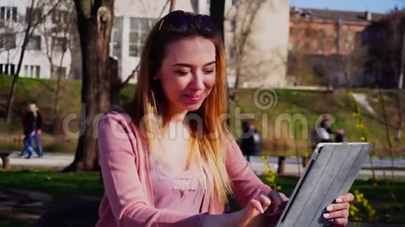 美丽的女性在公园里通过平板电脑与朋友聊天视频的预览图