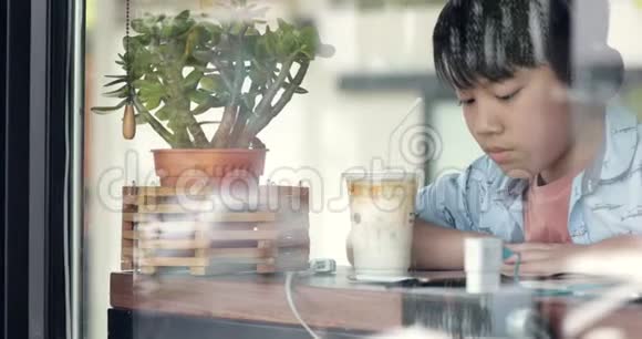 亚洲可爱的男孩用手机在杯子里喝牛奶微笑概念社交网络消息技术视频的预览图