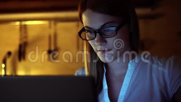 漂亮迷人的女人戴着眼镜在笔记本电脑上浏览互联网晚上厨房喝咖啡视频的预览图