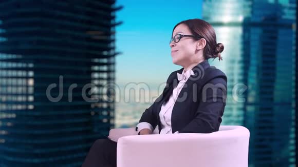 电视演播室戴眼镜的深色头发她穿着西装坐在工作室里接受采访微笑和微笑视频的预览图