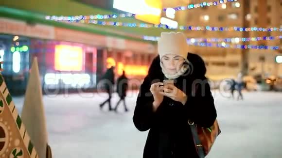 一位穿着毛皮大衣的年轻女子在街上的一棵树旁写短信视频的预览图