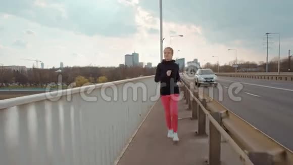 穿着运动服的年轻女子正在城市背景下的一座桥上奔跑视频的预览图