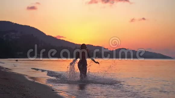 快乐的黑发年轻女子在令人惊叹的日落中缓慢地奔跑在热带海滩上1920x1080视频的预览图