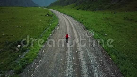 空中飞行年轻迷人的女徒步旅行者带着背包在山上的一条土路上女旅行者西伯利亚阿尔泰视频的预览图