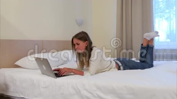 一个体贴的金发女人她用笔记本电脑躺在酒店房间的床上视频的预览图