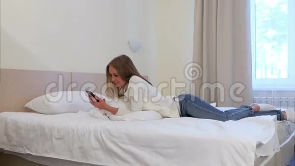 微笑的女人在躺在酒店的床上时使用手机视频的预览图