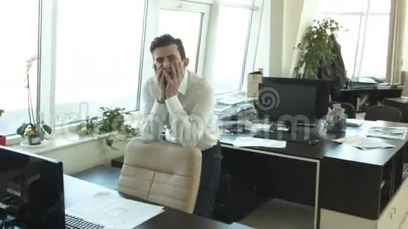 一位年轻的商人在办公室为一位朋友欢呼视频的预览图