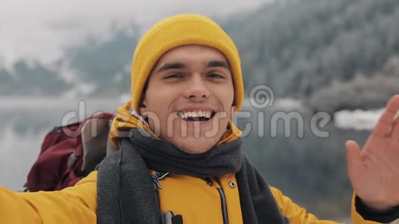 英俊的徒步旅行者在智能手机上打电话对着相机挥手微笑着和朋友说话美丽的冬天视频的预览图