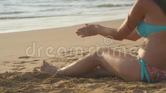 美丽的女孩坐在沙滩上的金沙上在暑假旅行中放松年轻妇女的手臂视频的预览图