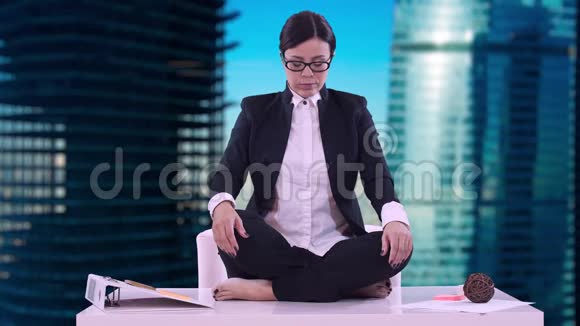 办公室里年轻商务女性的肖像她坐在桌上坐在莲花的位置上沉思着做生意视频的预览图