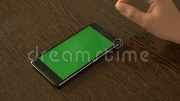 一只女手和一部手机上面有一个绿色的屏幕躺在桌子上视频的预览图